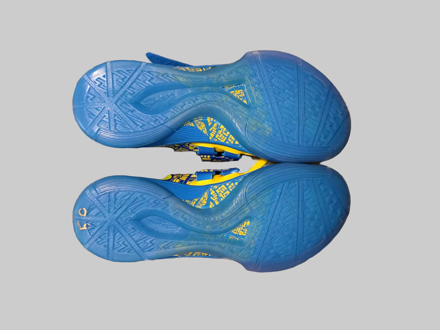 A pair of blue athletic shoes shown from the sole side, resting on a plaid blanket with a person's hand visible underneath for scale.
