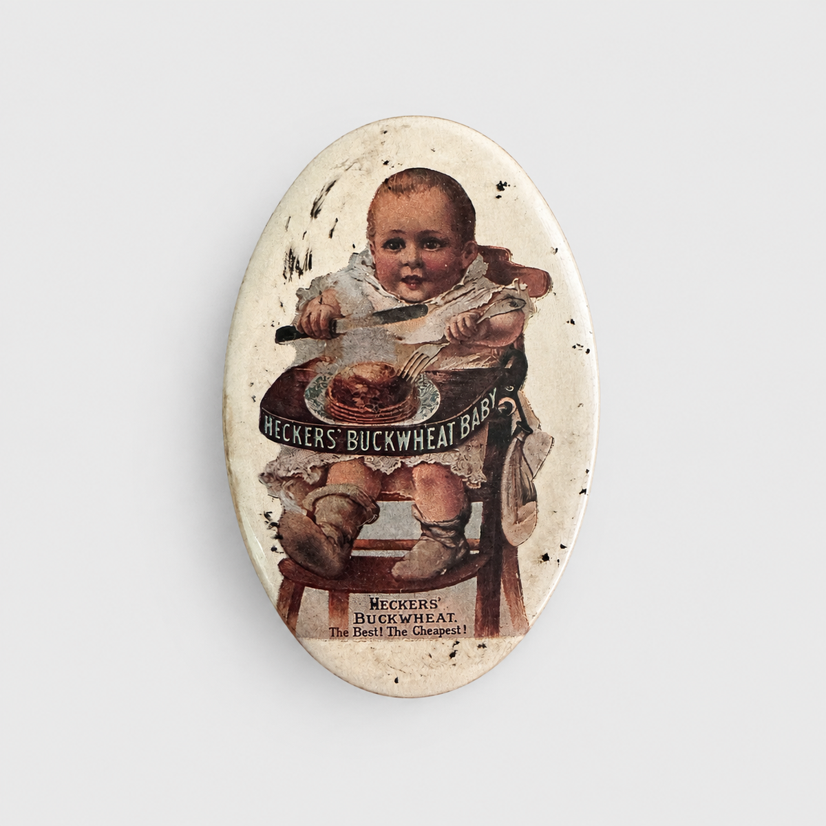 An oval vintage-style collectible pinback button featuring a retro illustration of a baby in a high chair with a plate of buckwheat, surrounded by distressed speckles and the text 'HECKERS' BUCKWHEAT'.