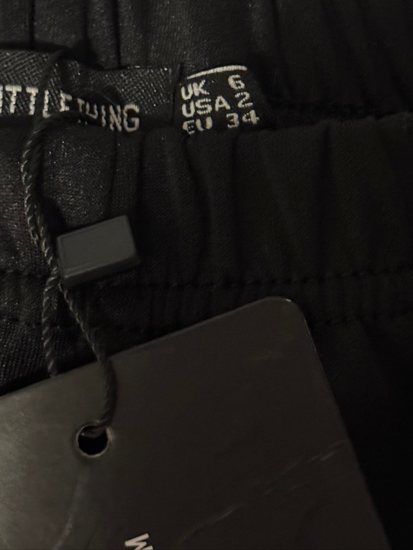 Close-up of black pants with size tags on a textured surface