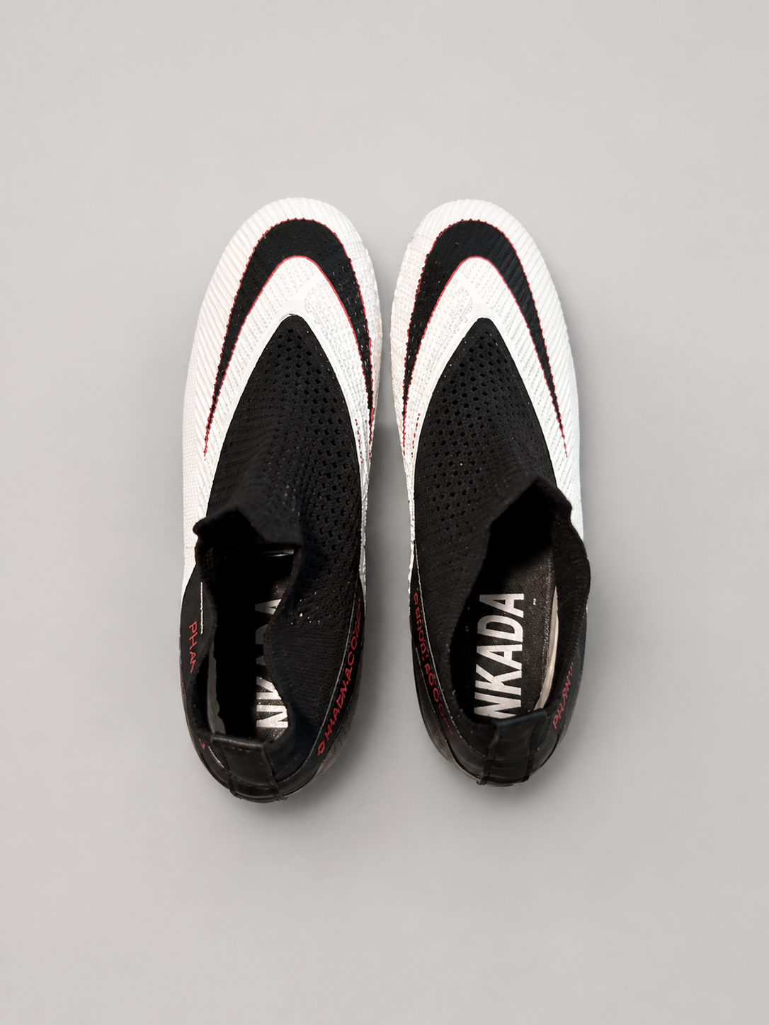 A pair of black and white slip-on sneakers with red accents, viewed from a top-down perspective on a neutral gray background.