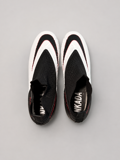 A pair of black and white slip-on sneakers with red accents, viewed from a top-down perspective on a neutral gray background.