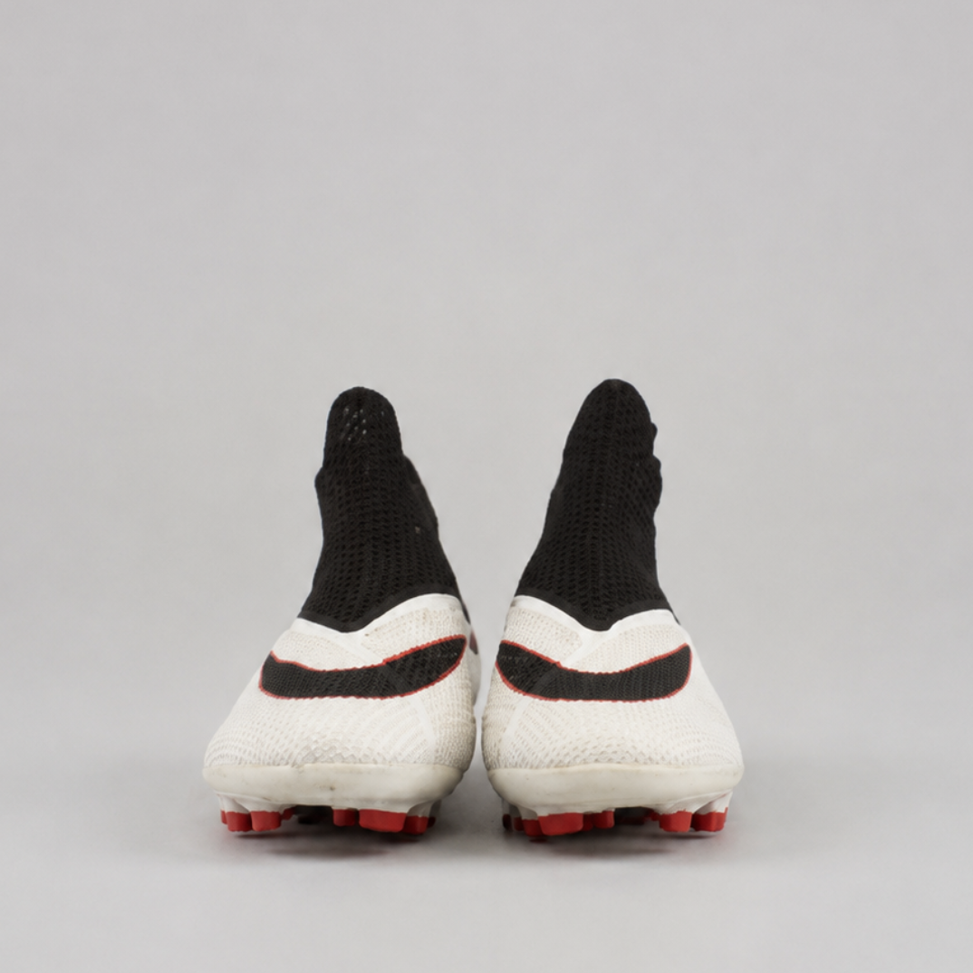 A pair of soccer cleats shown from the back, featuring a white knit upper with black accents, a black swoosh design, and red studs on a light gray background.