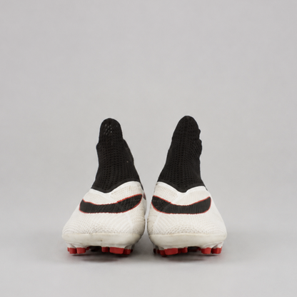 A pair of soccer cleats shown from the back, featuring a white knit upper with black accents, a black swoosh design, and red studs on a light gray background.