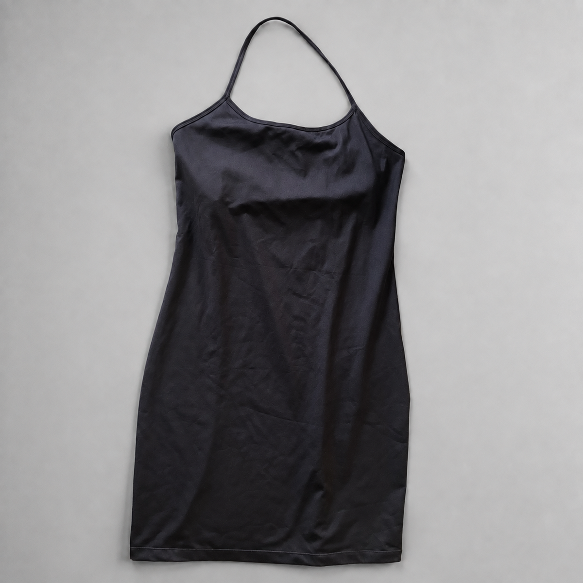 A black athletic dress with thin spaghetti straps, laid flat on a neutral gray background.