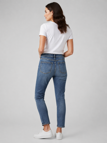 A woman is shown from the back wearing blue skinny jeans, a white t-shirt, and white sneakers against a light gray studio background.
