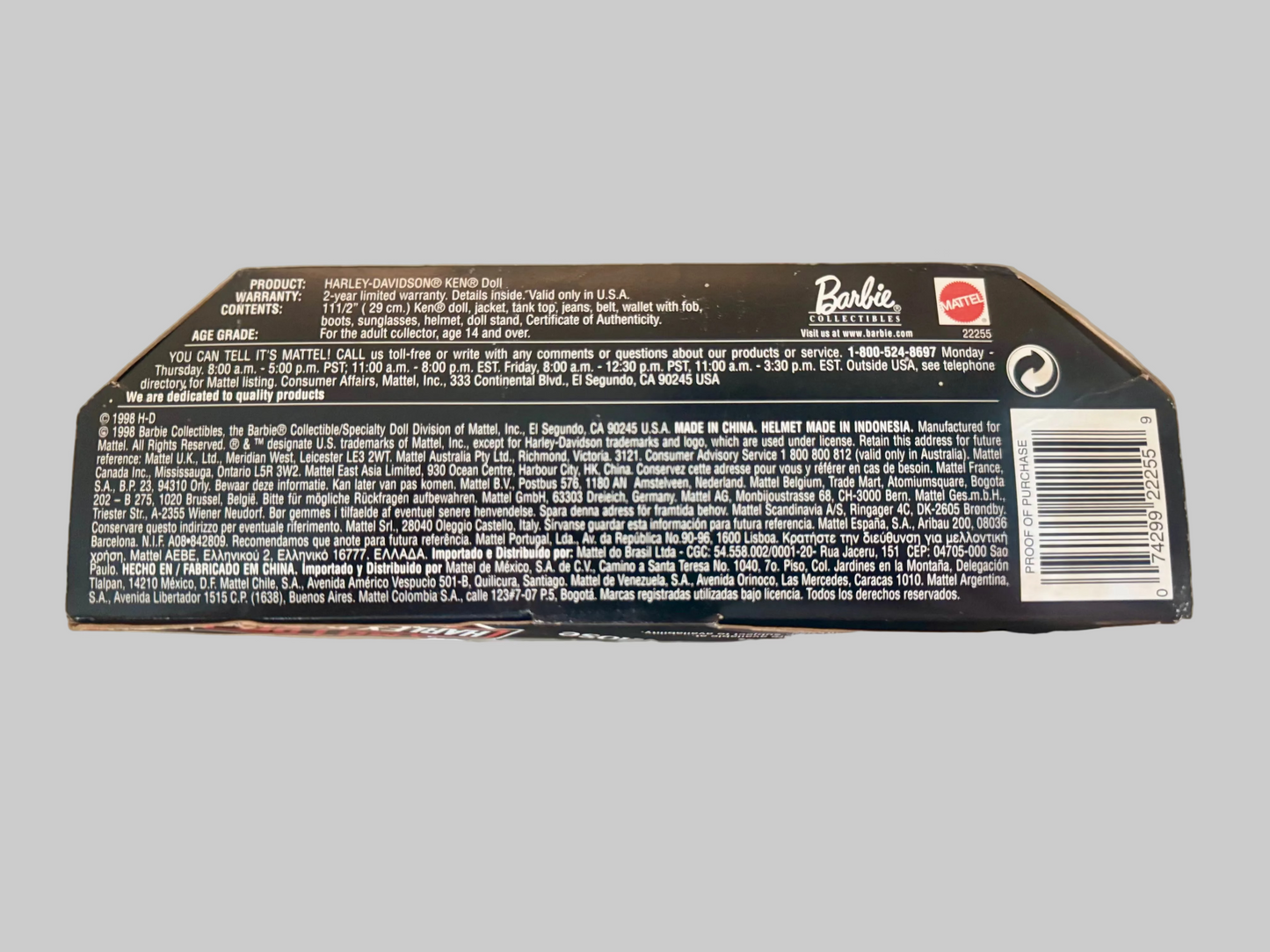 The back of a Barbie-branded product box, showing printed text, a barcode, and a small red Barbie logo, photographed against a blurred indoor background.