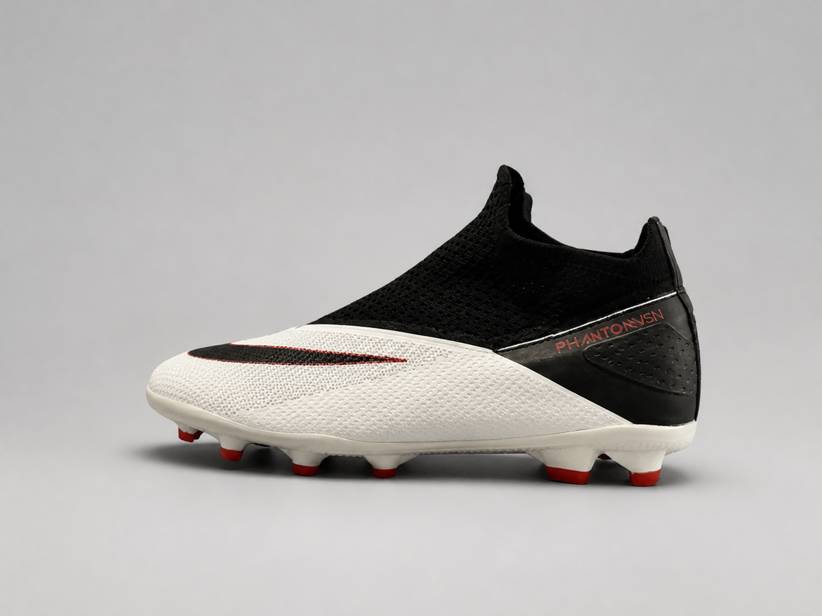 A Nike soccer cleat in white and black with red accents, featuring a knit upper, a black swoosh, and red studs, shown against a neutral gray background.