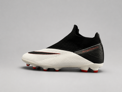 A Nike soccer cleat in white and black with red accents, featuring a knit upper, a black swoosh, and red studs, shown against a neutral gray background.