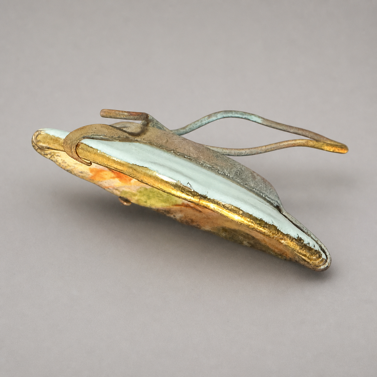 An abstract sculptural art piece featuring a curved, metallic gold and silver base with a light blue-green glazed center, photographed on a neutral gray background.