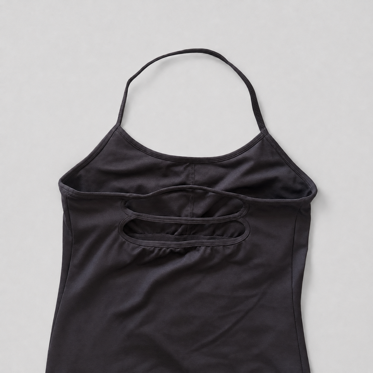 A black sleeveless camisole top with a double-strap back design and a small side pocket, laid flat on a light gray background.