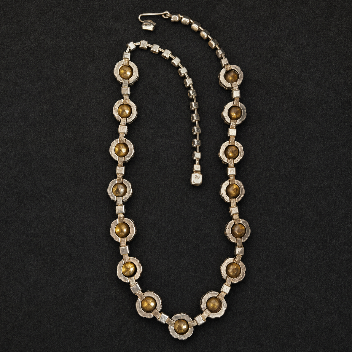 A vintage silver-tone necklace featuring circular brown and gold tiger's eye beads set in textured silver bezels, displayed on a dark textured background.