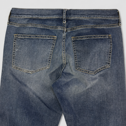 Close-up back view of blue denim jeans showing the waistband, belt loops, and back pockets on a light gray background.