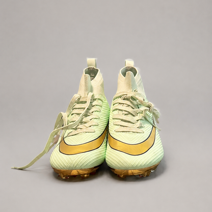 A pair of  high-top soccer cleats in pale mint green and gold, shown from the front on a neutral gray background.