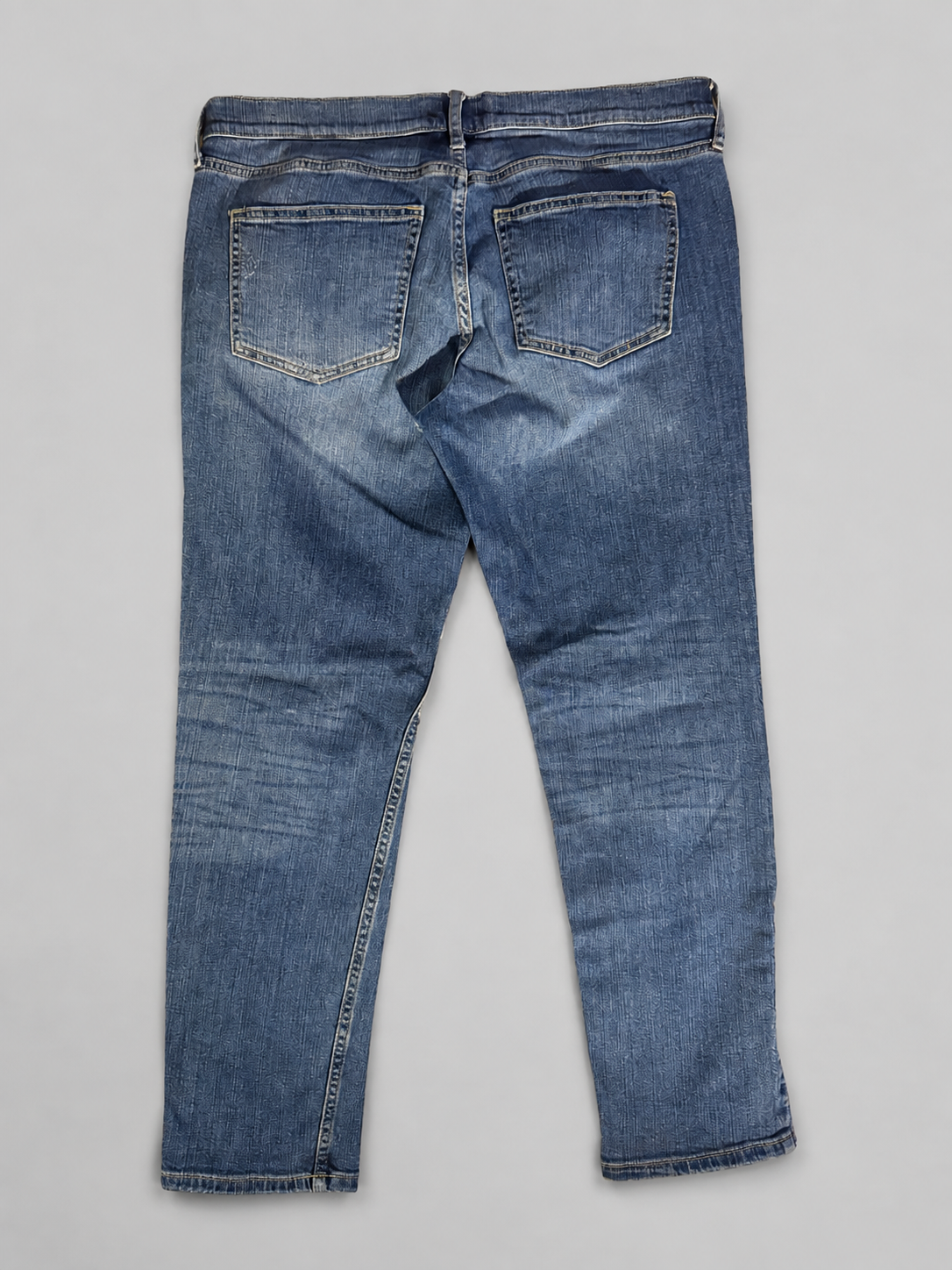 Back view of a pair of medium-wash blue denim jeans on a light gray background.