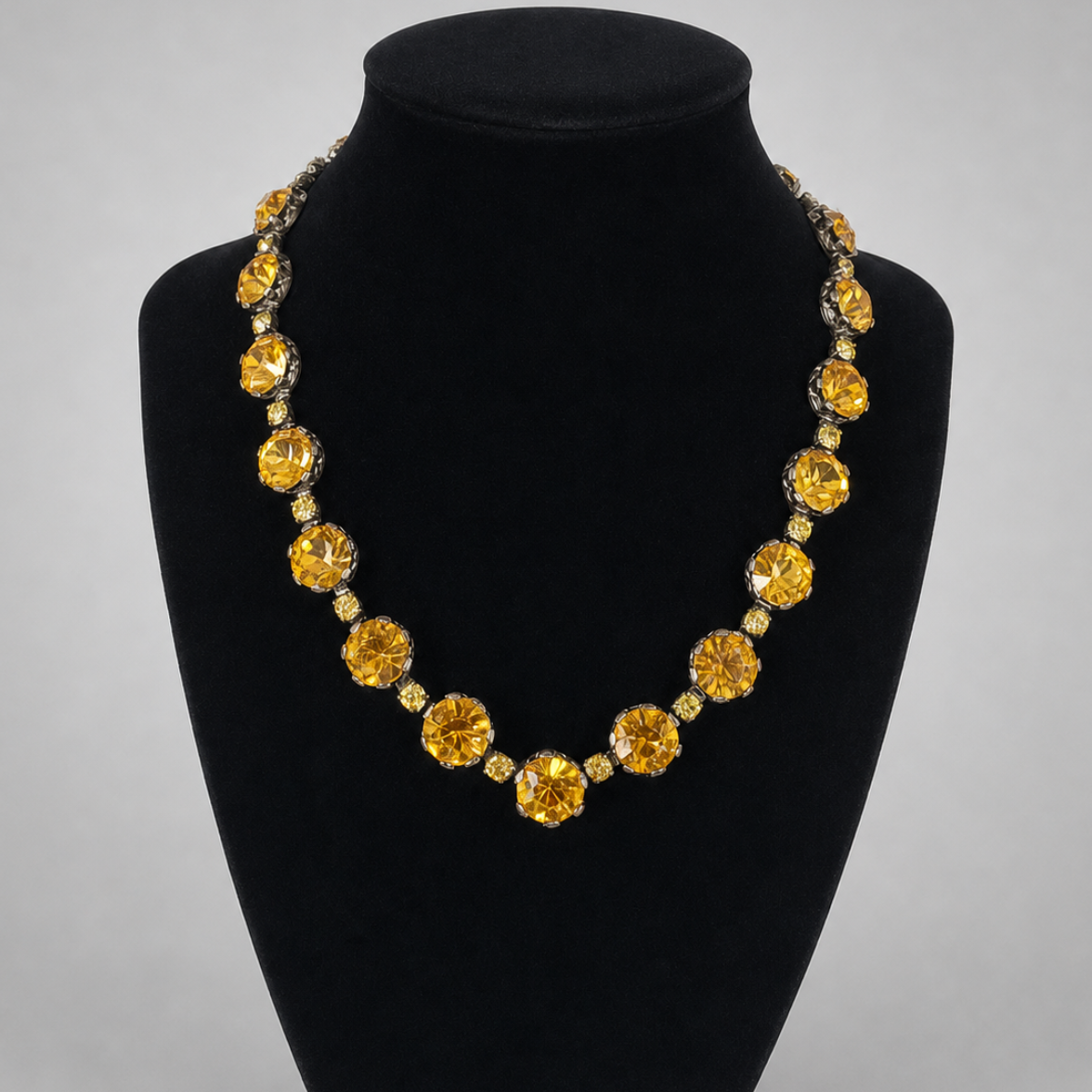 A statement necklace featuring large round yellow gemstones and smaller clear accent stones, displayed on a black velvet jewelry bust against a light gray background.