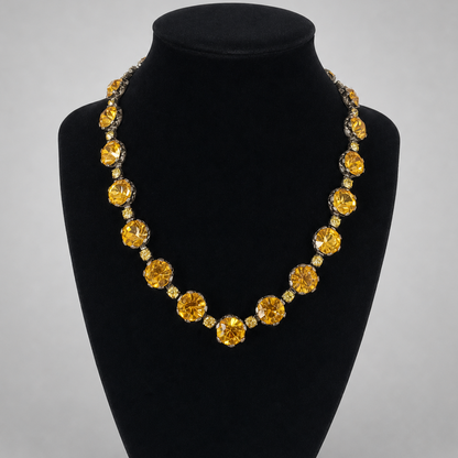 A statement necklace featuring large round yellow gemstones and smaller clear accent stones, displayed on a black velvet jewelry bust against a light gray background.