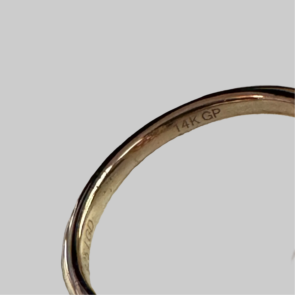 A yellow gold ring featuring a large, cushion-cut pink gemstone in a prong setting, surrounded by a halo of small clear stones, displayed on a light off-white background.