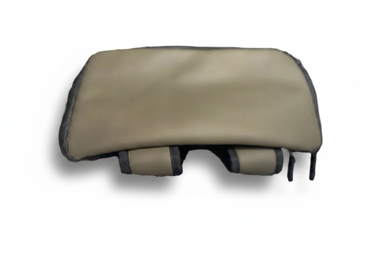 A beige massage pillow with black trim and adjustable straps, resting on a textured light gray blanket in a blurred indoor setting.