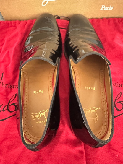 Black patent leather loafers on a red surface with 'Paris' branding.
