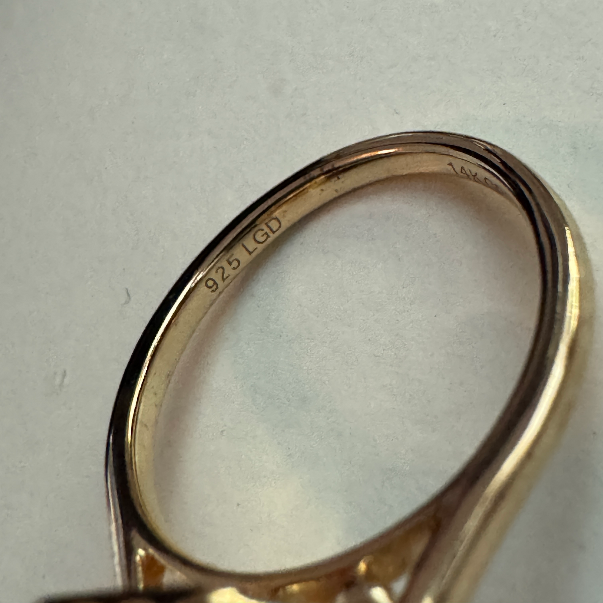 Close-up of the inside of a yellow gold ring, showing a 925 LTD sterling silver purity stamp engraved on the band, set against a light gray background.