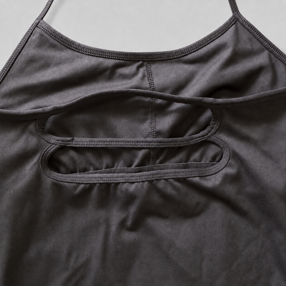 Close-up of a dark gray athletic tank top showing the back straps and double cutout details.