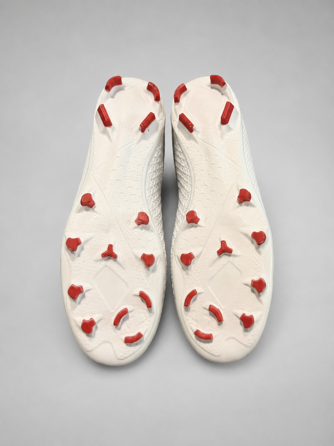 A pair of white soccer cleats shown from a top-down view, highlighting the white outsole with red conical studs.