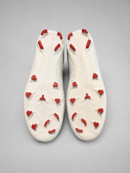 A pair of white soccer cleats shown from a top-down view, highlighting the white outsole with red conical studs.