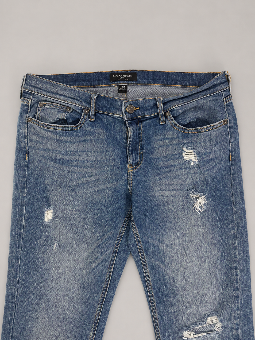 Light blue distressed denim jeans with ripped details on the thighs and knees, laid flat against a neutral gray background.