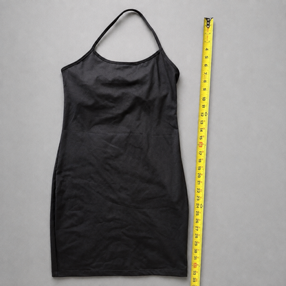 A black halter-neck dress or apron-style garment laid flat on a gray background, shown next to a yellow measuring tape for scale.