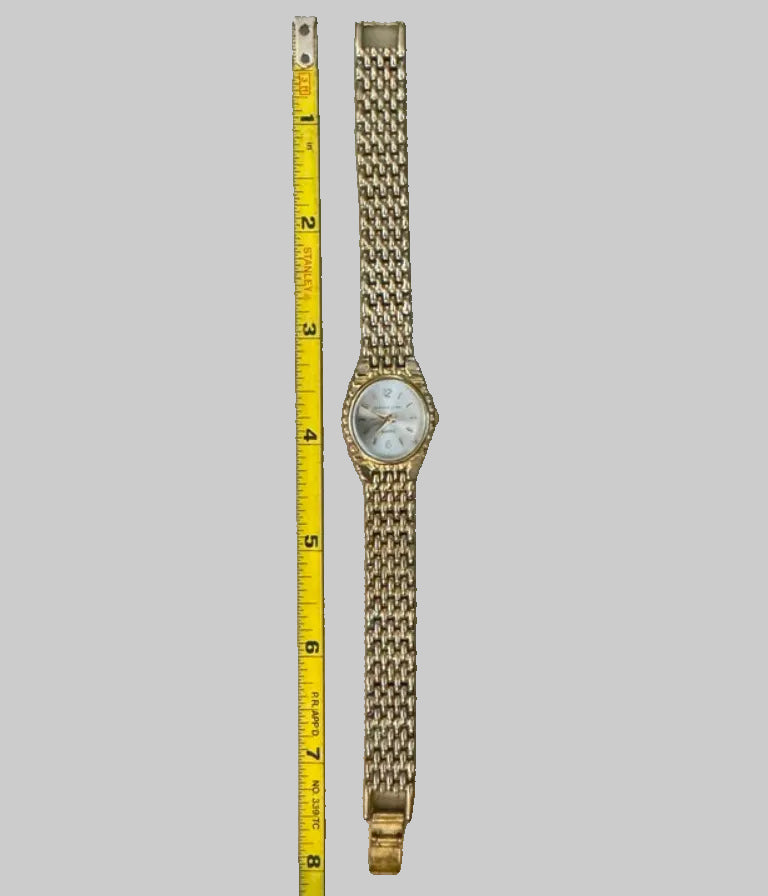 Gold watch with chain strap next to a tape measure on a concrete surface