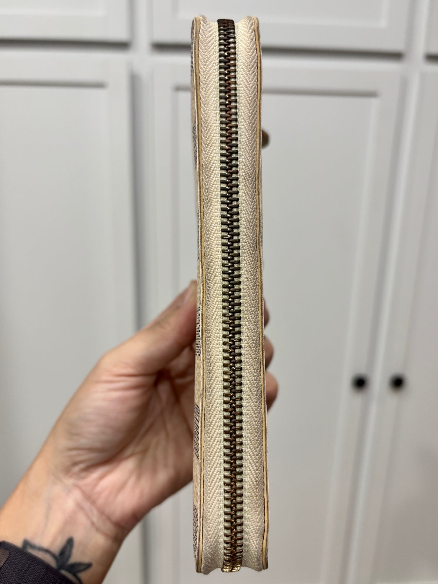 Hand holding a beige clutch with a zipper against a gray background