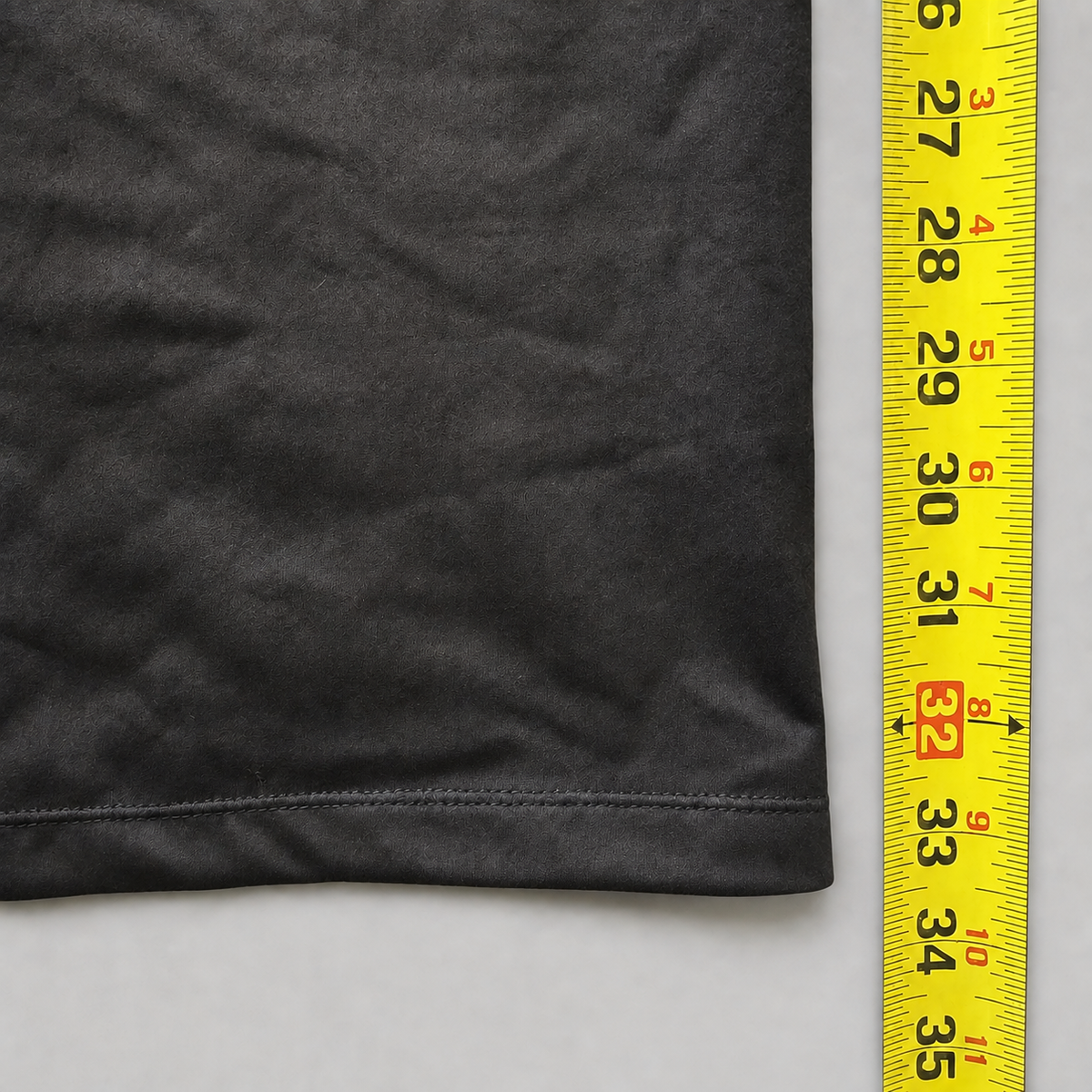 A close-up of a dark gray fabric item with a hemmed edge next to a yellow measuring tape to show the size.