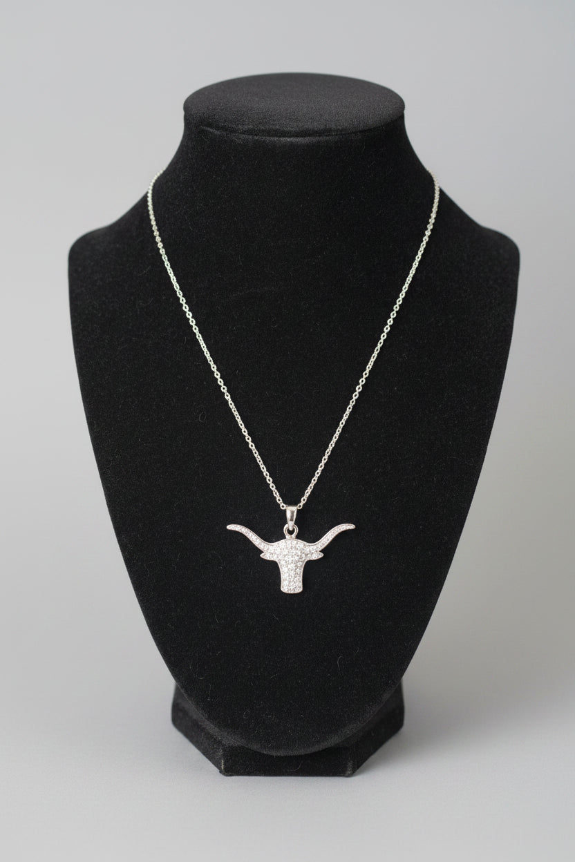 A silver-toned chain necklace with a longhorn-shaped pendant displayed on a black velvet jewelry bust, set against a blurred indoor background.