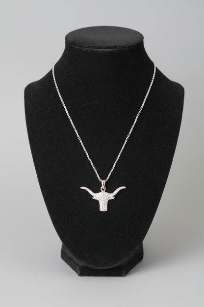 A silver-toned chain necklace with a longhorn-shaped pendant displayed on a black velvet jewelry bust, set against a blurred indoor background.
