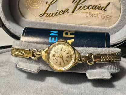 Gold wristwatch with chain on a gray surface, branded 'Lucien Piccard'.