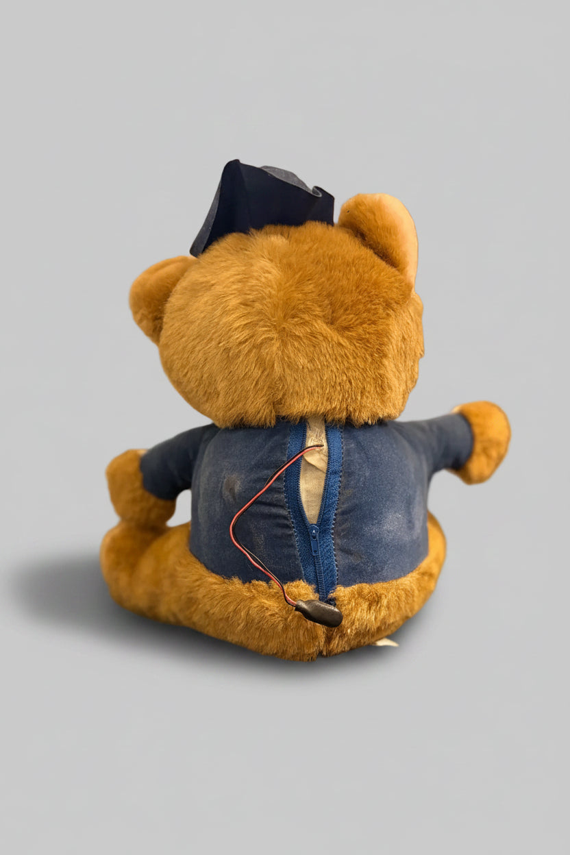 Brown teddy bear wearing a blue jacket on a dark surface