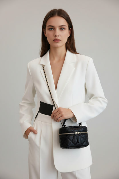 Black quilted handbag with chain strap worn by a person in a white outfit.