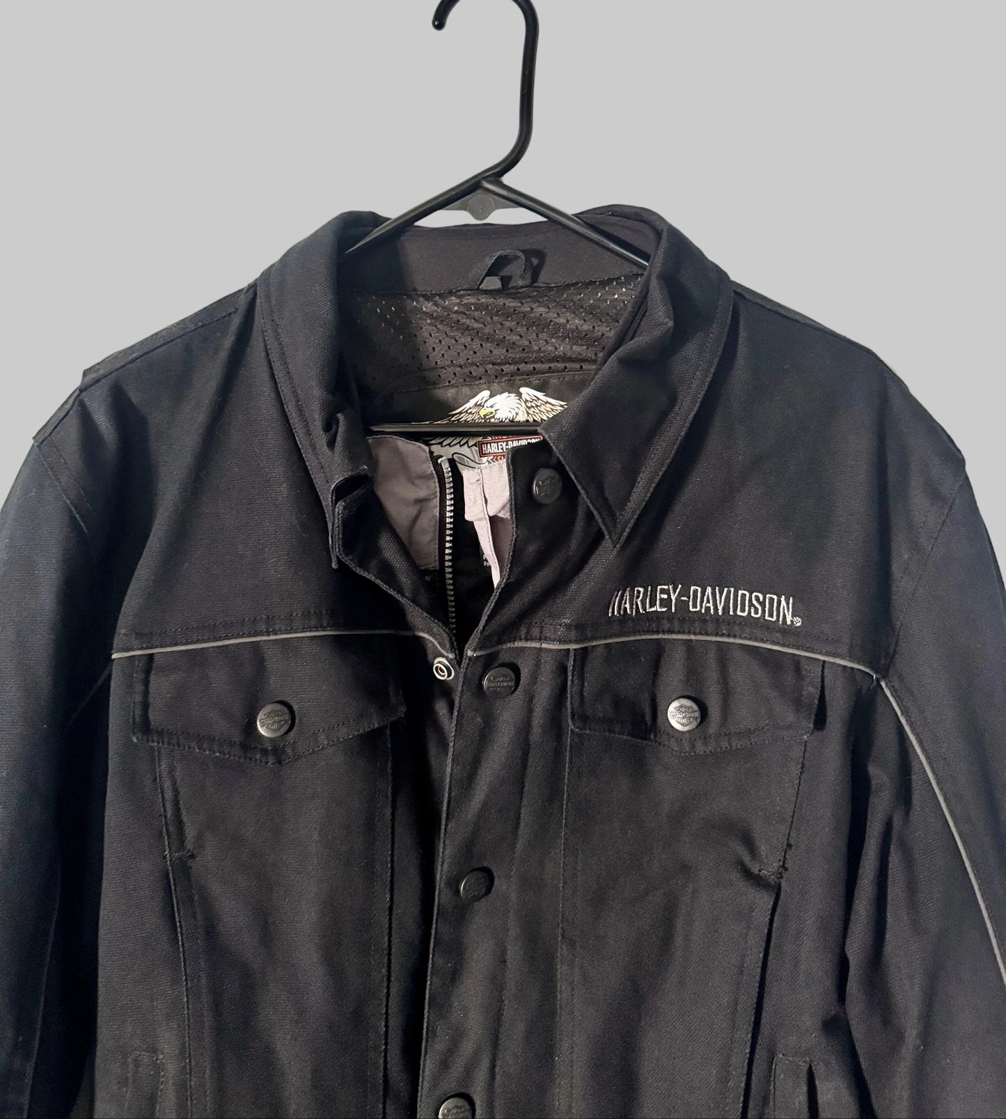 Black Harley-Davidson jacket on a hanger against a white door background