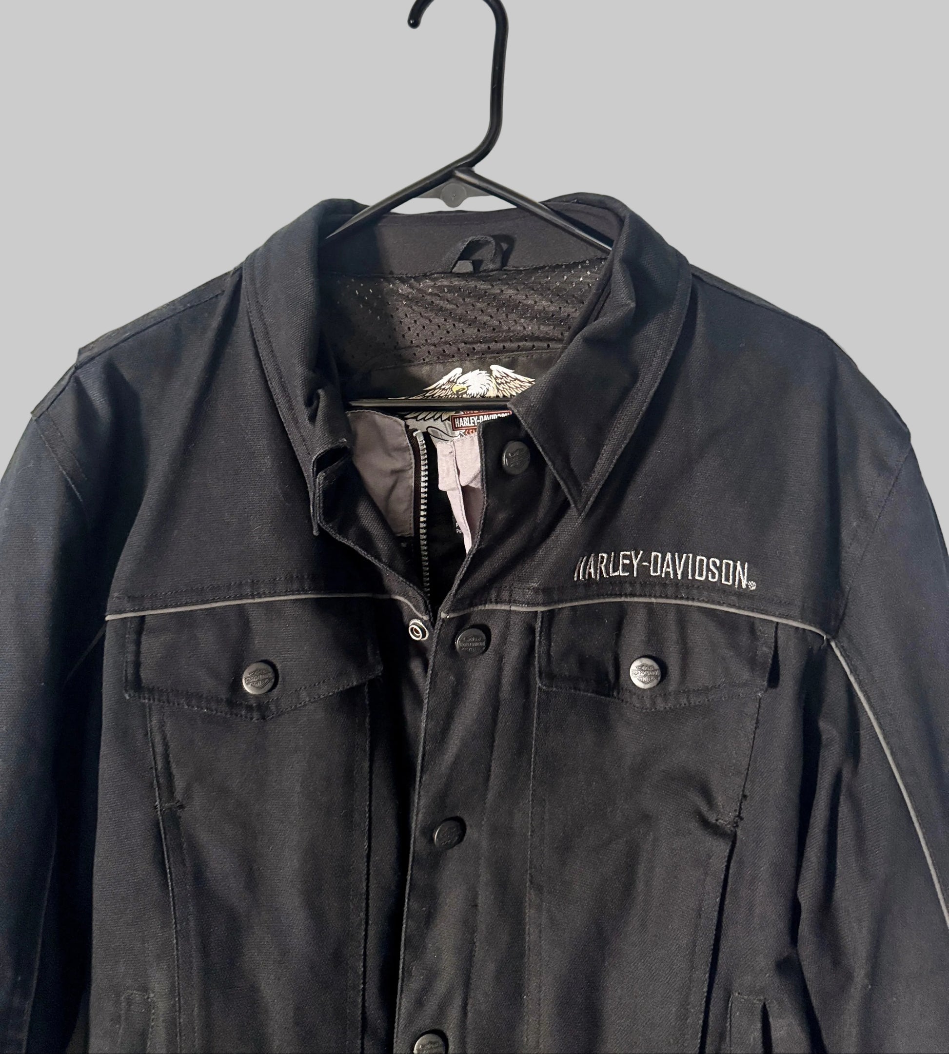 Black Harley-Davidson jacket on a hanger against a white door background