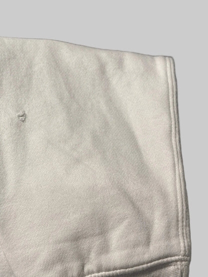 Close-up of a light gray sweatshirt sleeve with a visible seam and pocket detail, resting on a dark surface with part of a person's leg visible.