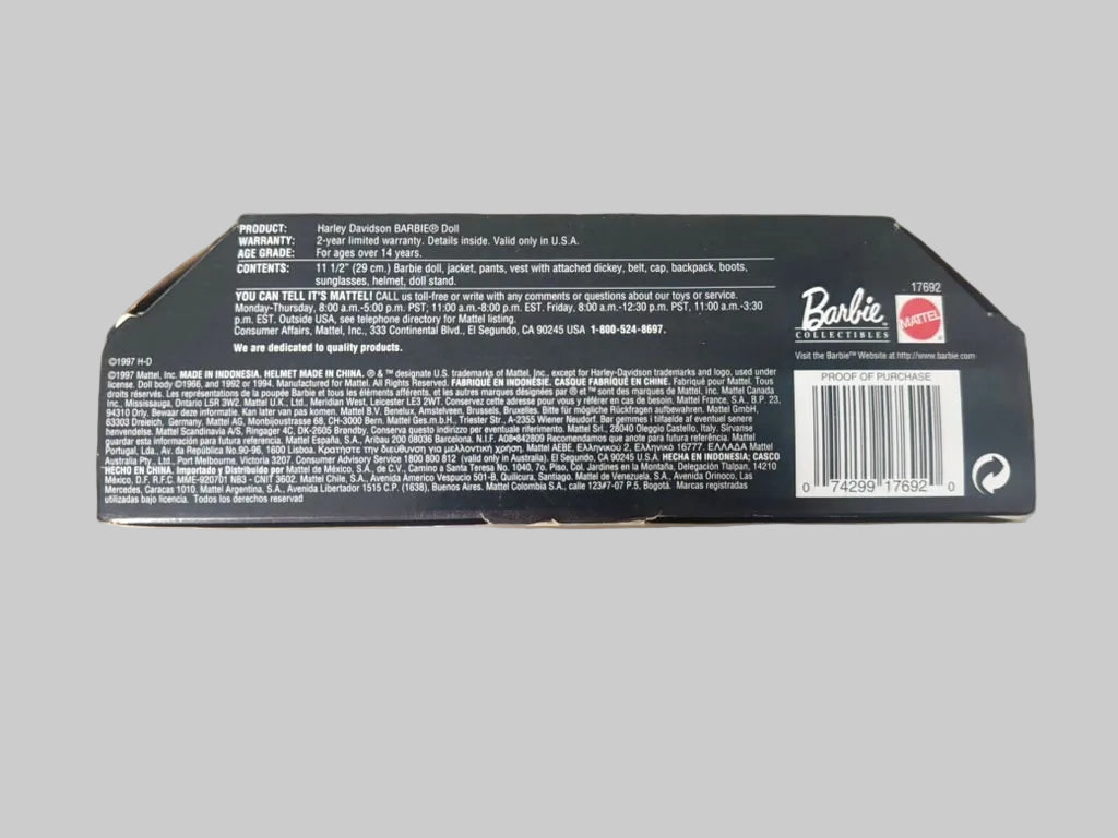 The back of a Barbie-branded product box, showing product information, a barcode, and the Barbie logo on a blurred indoor background.