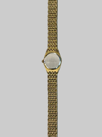 Back of Gold watch with a chain strap on a light gray surface