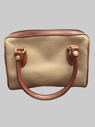 A small structured handbag in beige pebbled leather with brown leather trim and handles, resting on a dark wood floor.