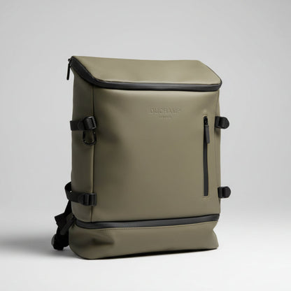 A light khaki canvas backpack with black trim and buckle straps, held by a hand in a bedroom setting.
