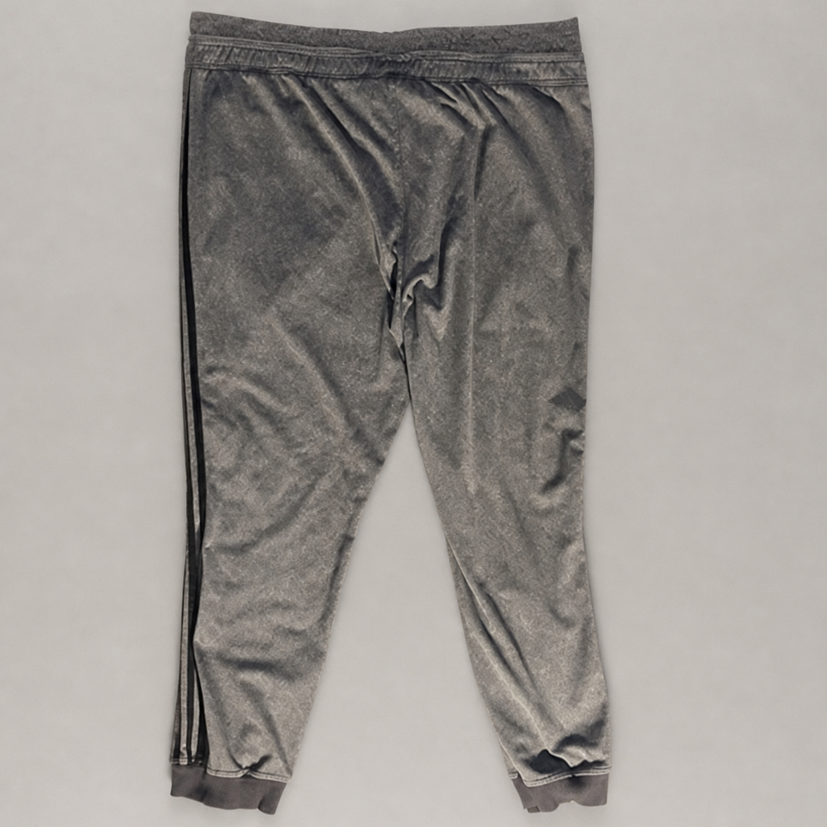 A pair of gray velvet jogger pants with black side stripes, laid flat on a light gray background.