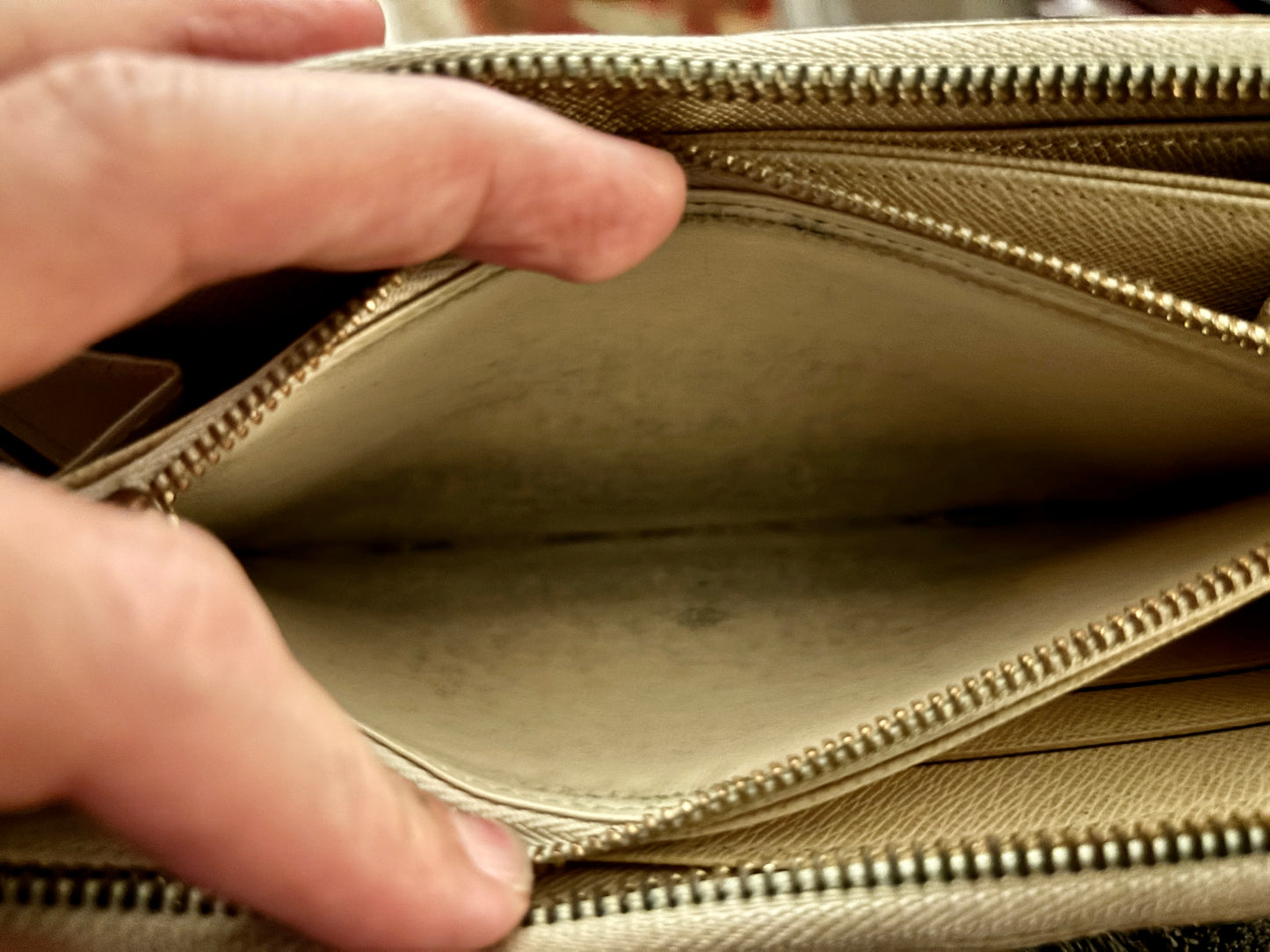 Close-up of a beige handbag with a zipper being pulled open by a hand.