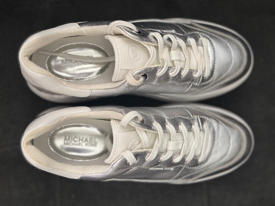 Pair of silver sneakers with white laces on a black background