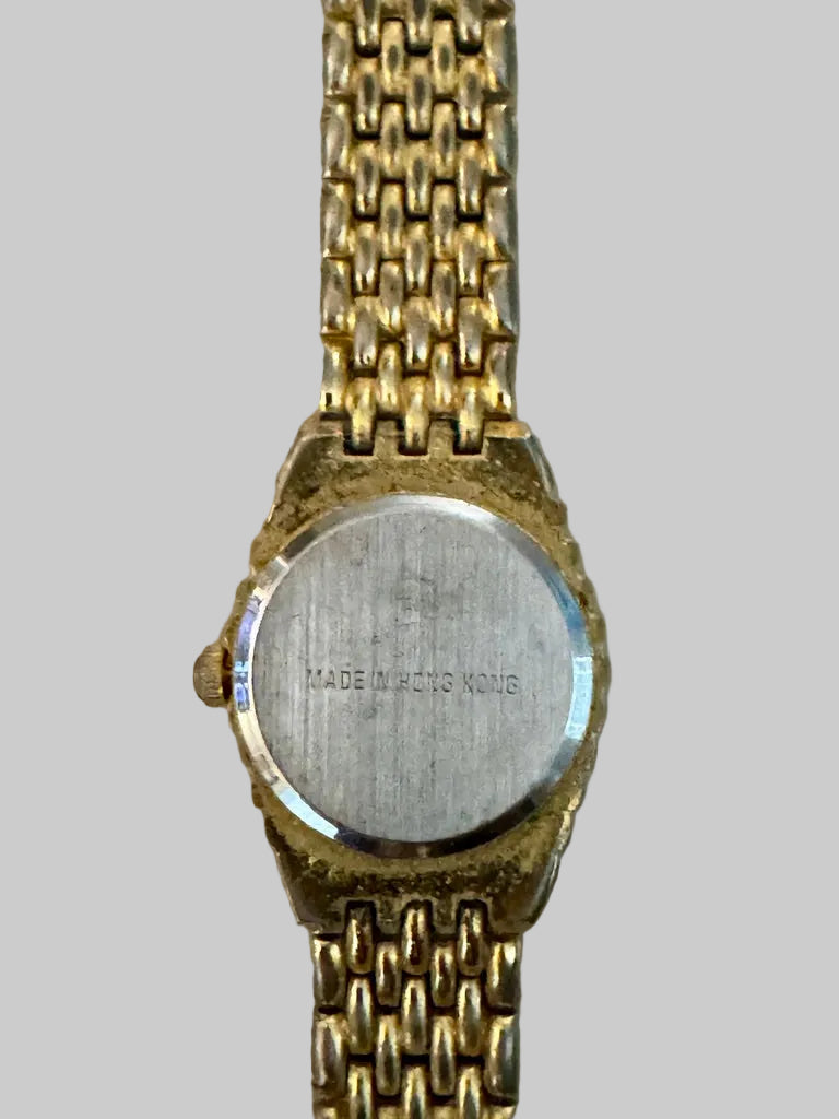 Back of Gold watch with 'MADE IN HONG KONG' engraving on a beige background