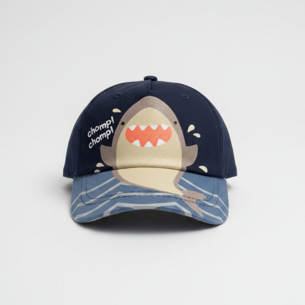 A dark navy blue baseball cap featuring a cartoon shark graphic on the brim and the text 'clown clomp!' on the side, resting on a gray shag rug.