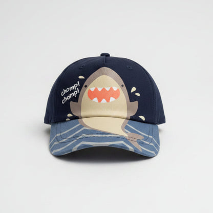 A dark navy blue baseball cap featuring a cartoon shark graphic on the brim and the text 'clown clomp!' on the side, resting on a gray shag rug.